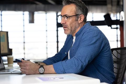 Middle-aged professional using smartphone and laptop in modern minimalist office interior