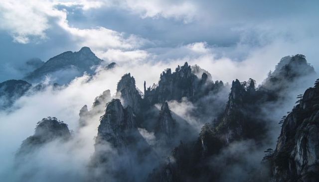 Jagged granite peaks rising through mist with windswept pines and dramatic clouds