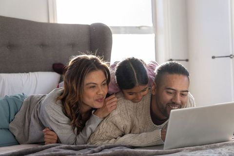 Family watching laptop together on bed sharing cozy moments and digital bonding, smiling