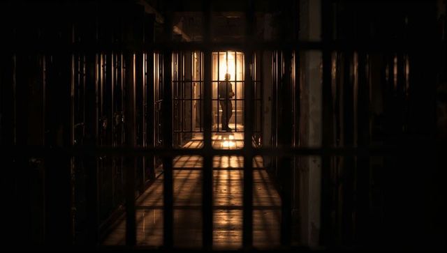 Silhouette in Dimly Lit Prison Corridor Behind Bars