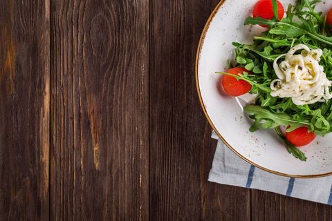 Fresh arugula and cherry tomato salad with shaved cheese on rustic wooden table