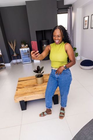 African american woman taking selfie in lime-green top at modern living room with plants
