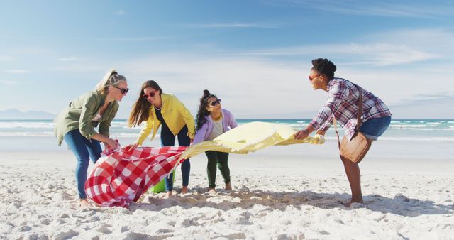 Happy group of diverse female friends having fun, preparing picnic at the beach. holiday, freedom and leisure time outdoors.