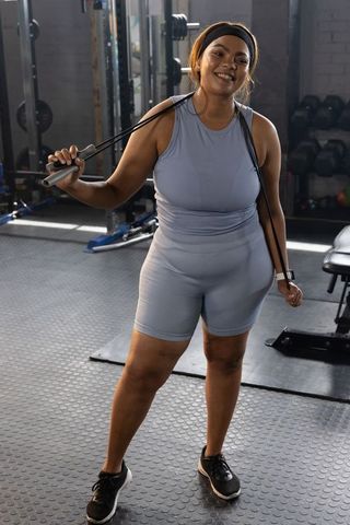 African american woman smiling holding jump rope wearing light blue workout set at gym