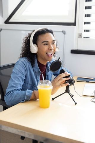Non-binary podcaster hosting lively home studio recording with headphones and microphone