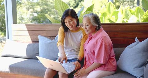 Young Woman Assisting Senior with Technology on Laptop Outdoors