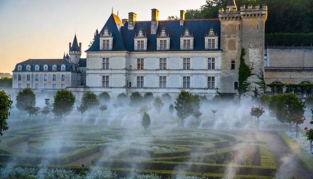 Misty loire valley stone chateau with crenellated tower and formal parterre garden at dawn