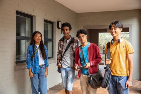 Diverse students collaborating outdoors with gadgets and bags