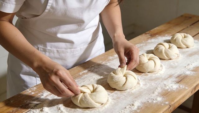 Baker shaping knotted artisan buns on floured wooden workbench