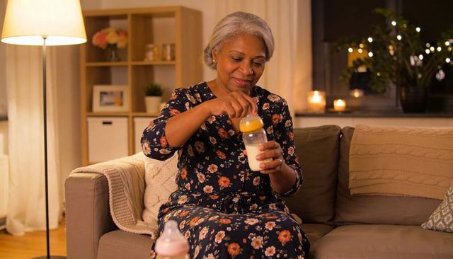 Grandmother preparing baby bottle on cozy sofa during evening feeding routine