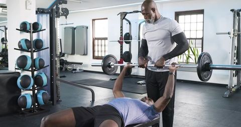 African american trainer coaching bench press technique in modern gym