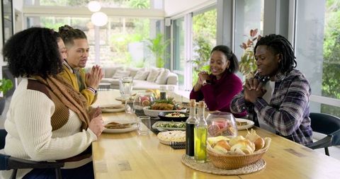 Diverse friends enjoying shared meal at wooden dining table in bright open living room