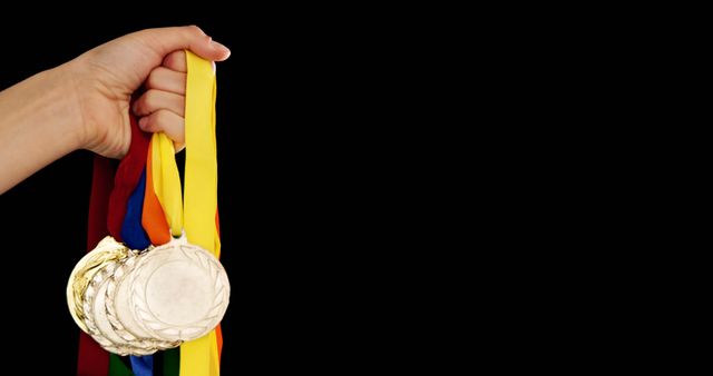 A hand is holding a collection of gold medals against a black background, with copy space - Download Free Stock Photos Pikwizard.com