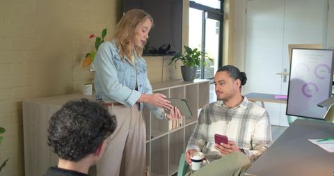 Coworkers Collaborating in Bright Modern Office Using Tablet and Smartphone Over Coffee