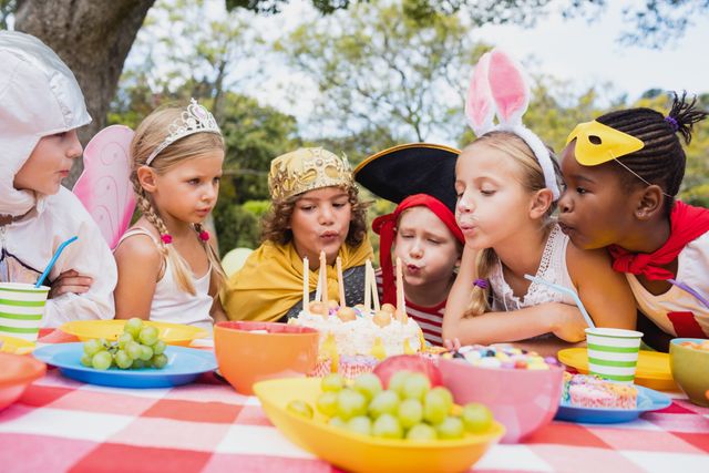  Cute children blowing together on the candle during a birthday party in the park