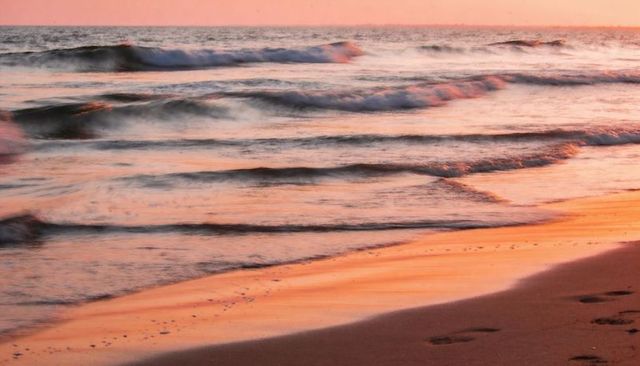 Pastel sunrise light lapping sandy shoreline with footprints and soft dawn reflection