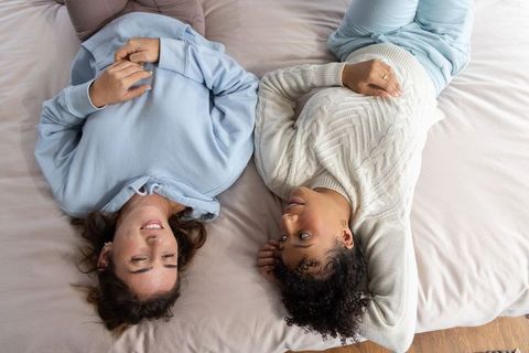Topdown two women lying on bed chatting in cozy cable-knit sweater and hoodie intimacy