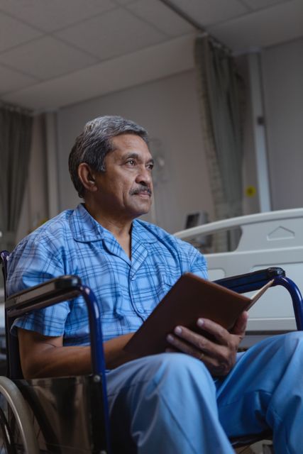 Senior man sitting in wheelchair reading book in hospital room. Ideal for healthcare, medical care, aging population, patient recovery, and hospital stay themes.