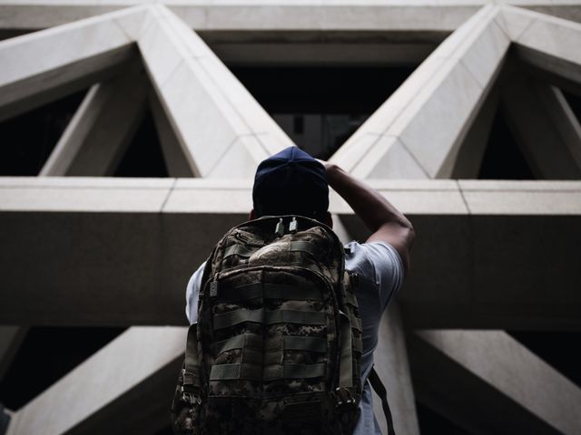 Individual with large backpack is capturing unique geometric architecture. Ideal for highlighting urban exploration, modern architecture, adventure seekers, or travel photography content. Useful in articles or advertisements about city adventures, exploration, or architecture studies.