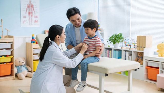 Pediatrician examining young boy with stethoscope during family clinic visit in pediatric room