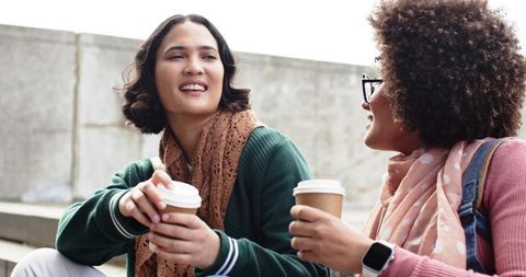Two friends chatting over takeaway coffee on concrete steps, casual urban meetup