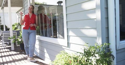 Smiling woman enjoying drink on sunny porch in red top and relaxed jeans