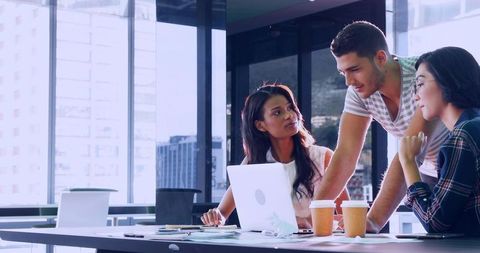 Young business team collaborating over laptop in high-rise office brainstorming session