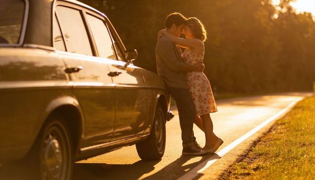 Sunset road romance: young couple embracing beside vintage sedan in warm golden light