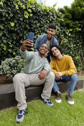 Group of teen friends taking selfie on backyard bench surrounded by lush green ivy wall