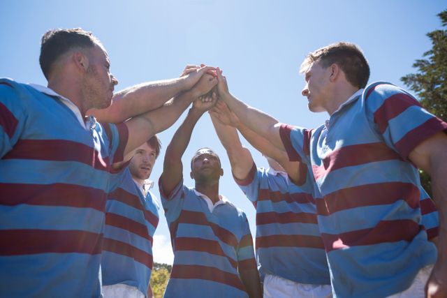Low angle view of rugby team with arms raised standing against sky