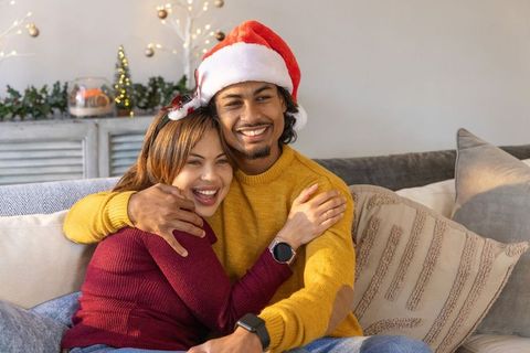 Cozy couple hugging on couch wearing santa hat, knit sweaters and smartwatches