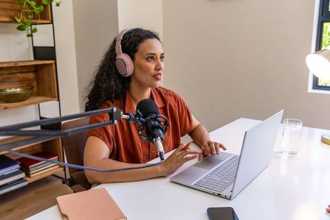 African american woman podcasting with laptop and studio microphone in modern home studio