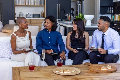 Diverse friends enjoying cocktail party with pizza in modern open-plan living room