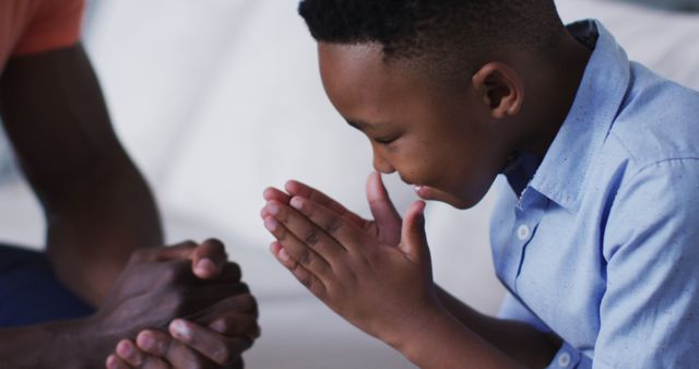 This visual captures a young boy in a moment of prayer with an adult beside him. The child's hands are clasped in prayer, implicating a spiritual or religious context. This can be used in content related to family, faith, spirituality, and prayer for blogs, articles, or religious publications.