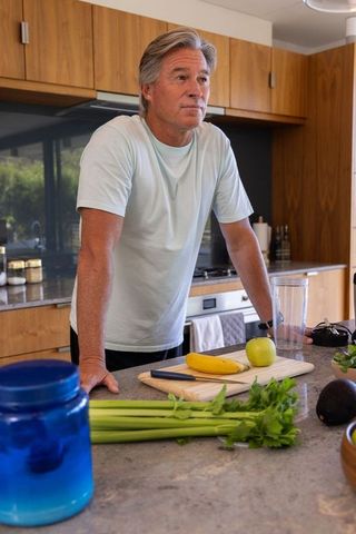 Senior man leaning on modern kitchen island arranging banana and celery for smoothie