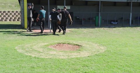 Baseball team gathering near dugout on worn pitcher's mound sunny field teamwork