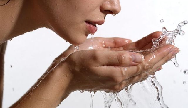 Woman cupping hands washing face with splashing water closeup wet skin beauty