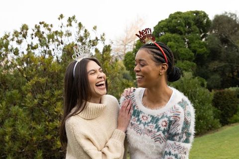 Laughing diverse friends wearing merry headbands in park celebrating holiday together