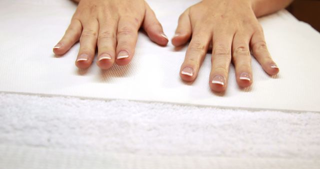 Depicts well-groomed hands with a neat French manicure resting on a white towel. Ideal for use in beauty, skincare, and spa industry advertisements. Also suitable for illustrating concepts of relaxation, hygiene, and hand care.