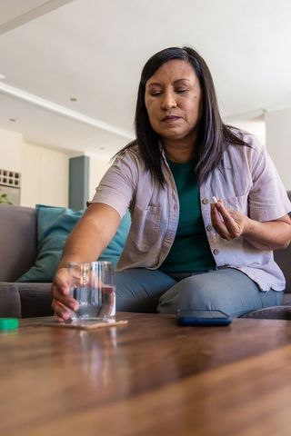 Senior woman taking pill and placing glass of water on coaster in tidy living room