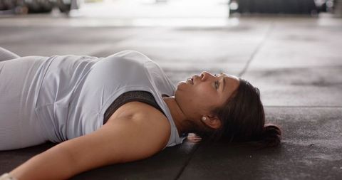 Asian woman lying on gym mat resting after intense workout, recovering and cooling down