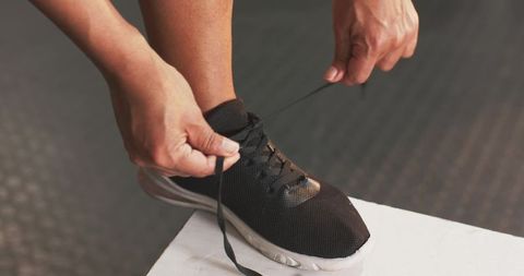 Woman tying black knit running shoe laces on white bench preparing for gym workout