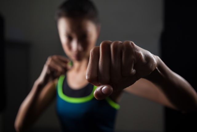 A determined woman practicing boxing in a fitness studio, showing focus and strength. Ideal for use in promoting fitness programs, gym memberships, women's self-defense classes, or motivational materials for sports and physical training.