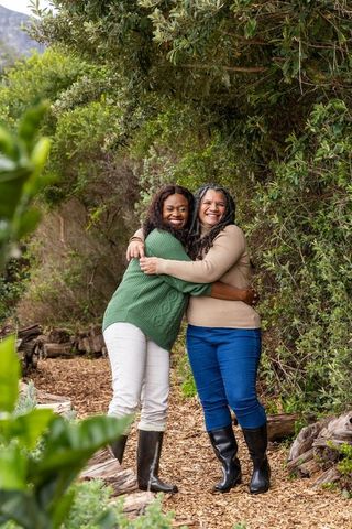 African american mature women hugging on forest trail wearing sweaters and rain boots