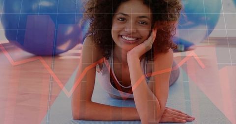 Smiling woman lying on yoga mat propping forearms in gym with red growth chart overlay