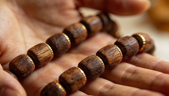 Hand holding wooden prayer beads with gold spacer rings macro closeup