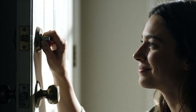 Woman unlocking deadbolt at home entryway in soft daylight