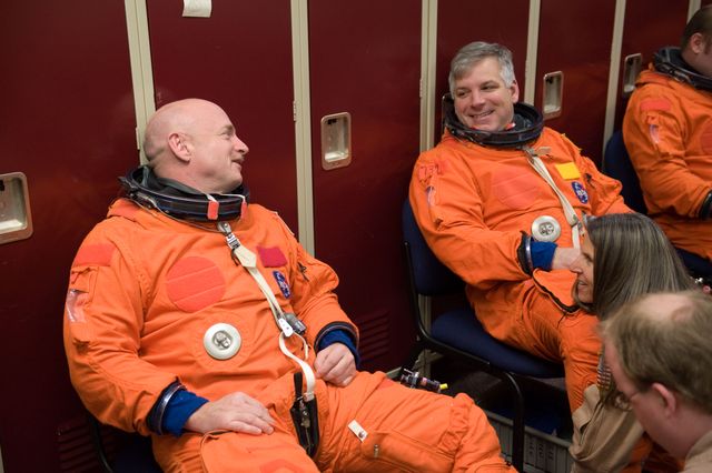 Two astronauts wearing orange shuttle launch and entry suits sitting and preparing for a training session in the Space Vehicle Mock-up Facility at NASA's Johnson Space Center. This image can be used in contexts related to space exploration, teamwork, NASA missions, and astronaut training programs.