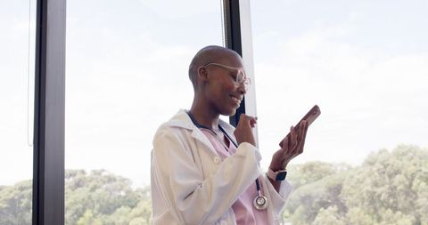Clinician dictating patient notes on smartphone while smiling by sunlit window