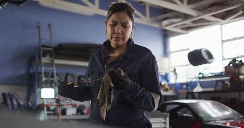 Inspecting female mechanic holding oily dipstick and rag in automotive repair garage